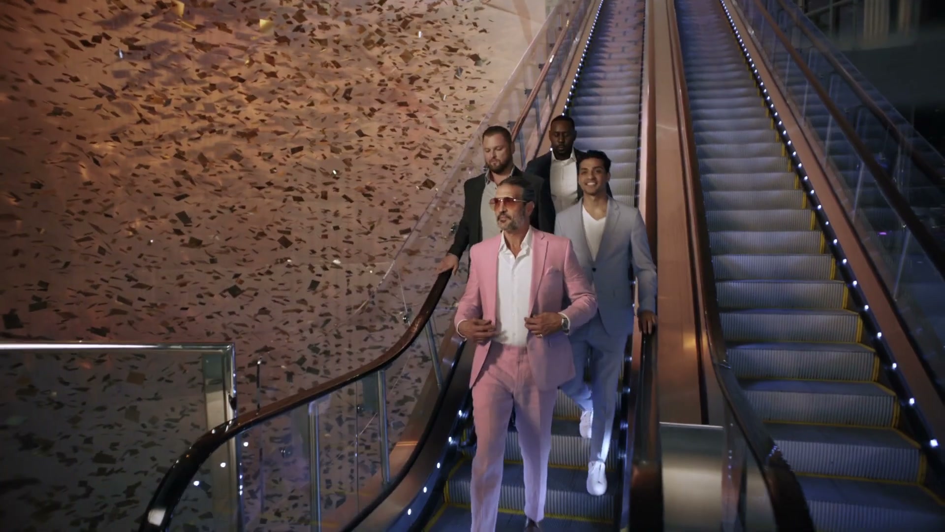 A crew descending an escalator through falling gold confetti, opening-night energy